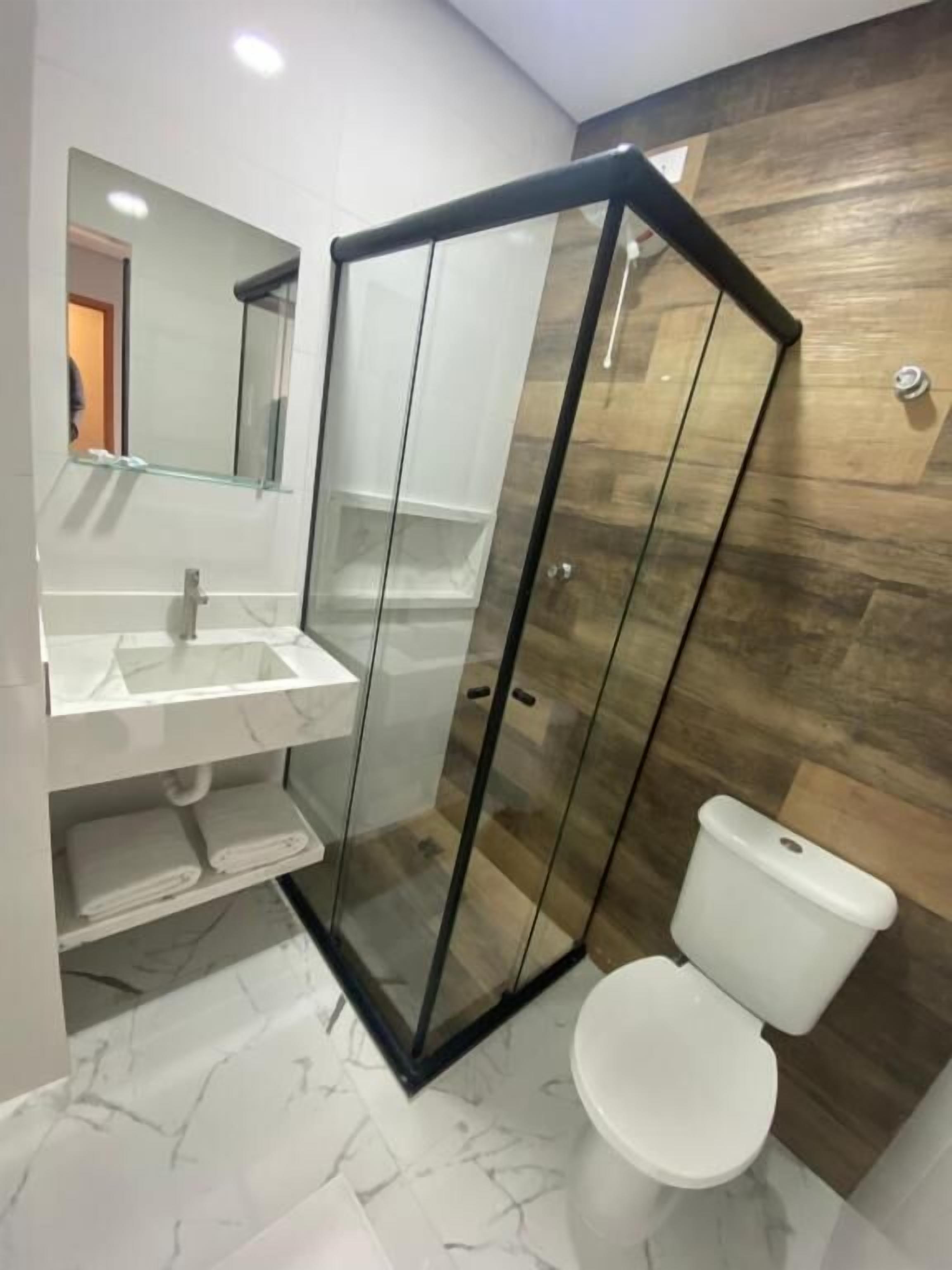 Un bany modern amb dutxa de vidre, un lavabo blanc i un vàter.