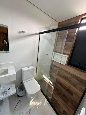 Un baño moderno con cabina de ducha de vidrio, inodoro blanco y piso de baldosas de mármol.