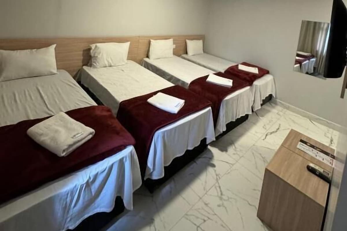 Habitación de hotel con cuatro camas individuales, un aparador de madera y un televisor de pantalla plana montado en la pared.