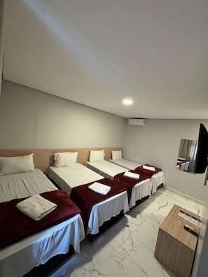 Habitación de hotel con cuatro camas individuales, un aparador de madera y un televisor de pantalla plana montado en la pared.