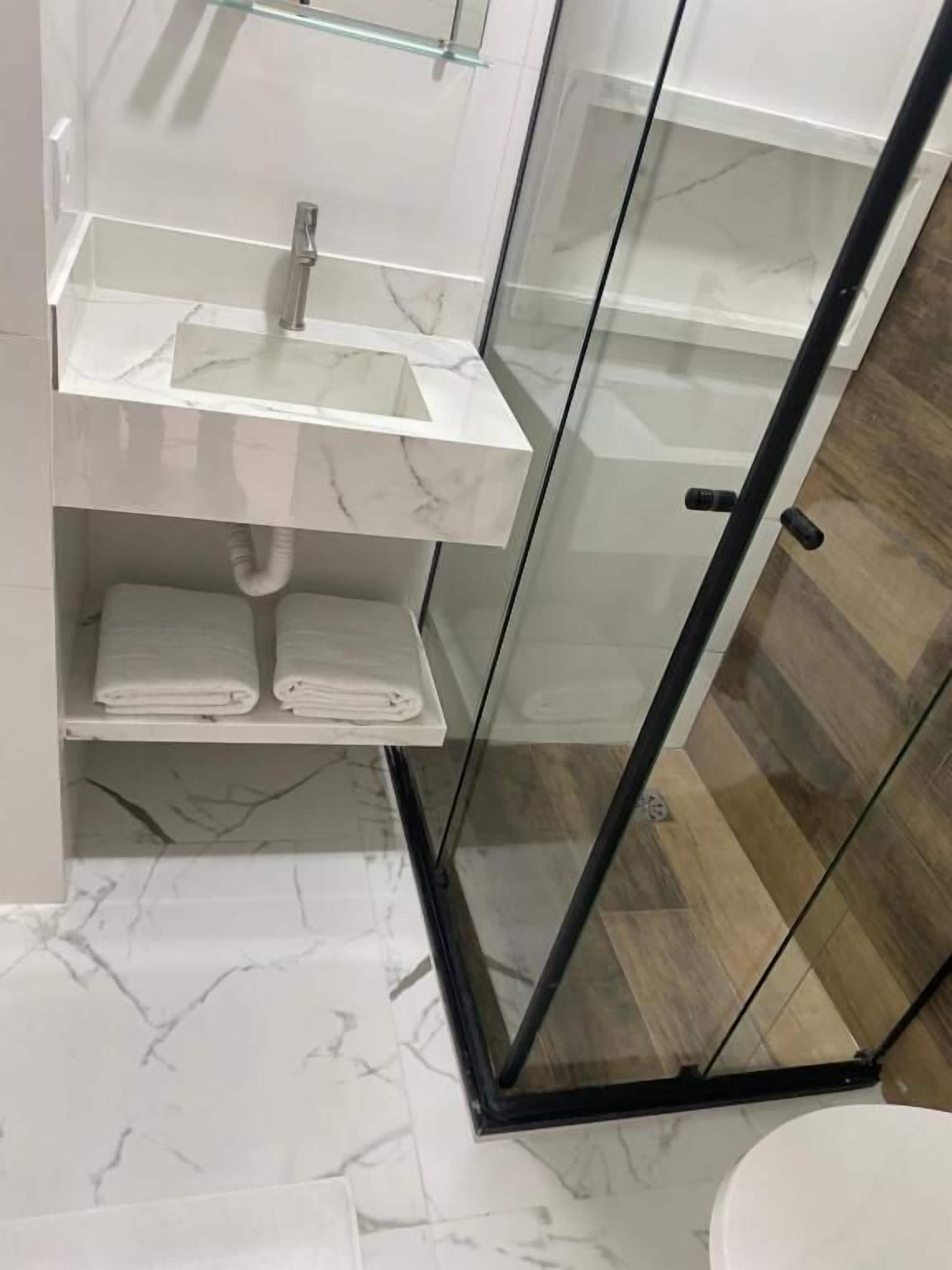 A bathroom with a glass shower enclosure, a white sink with a marble countertop, and a white toilet.