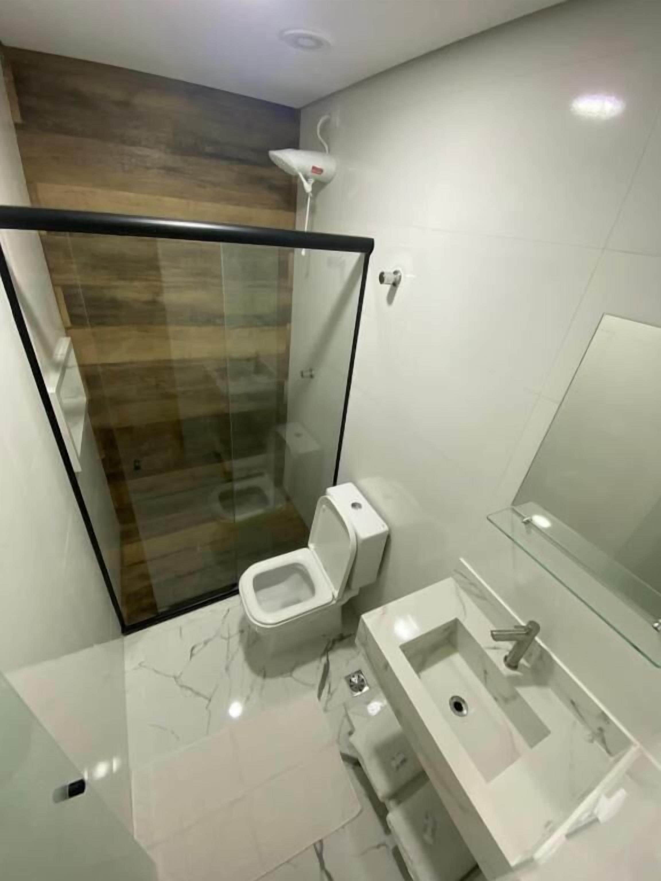 A modern bathroom with a glass-enclosed shower, a toilet, and a sink with a mirror.