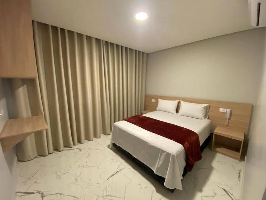 A hotel room with a bed, curtains, a bedside table, and a wall-mounted phone.