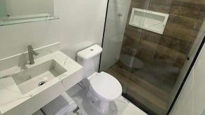 Un baño moderno con ducha de vidrio, un lavabo blanco y un inodoro.