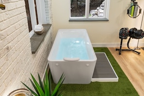 Une salle de spa équipée d’un jacuzzi, d’un porte-serviettes, d’une fenêtre donnant sur des rochers et d’un support pour haltères.