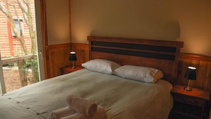 En säng med en enkel sänggavel i trä, två sänglampor och en hoprullad handduk på sängen.