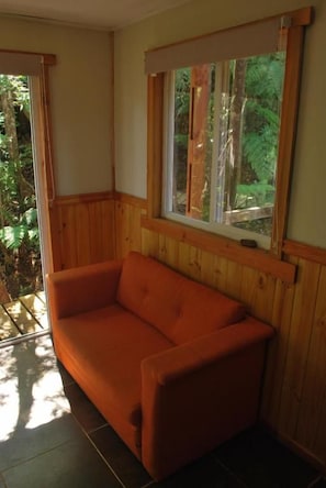 Habitació amb paret de fusta panelada, finestra amb vista a vegetació i un sofà.