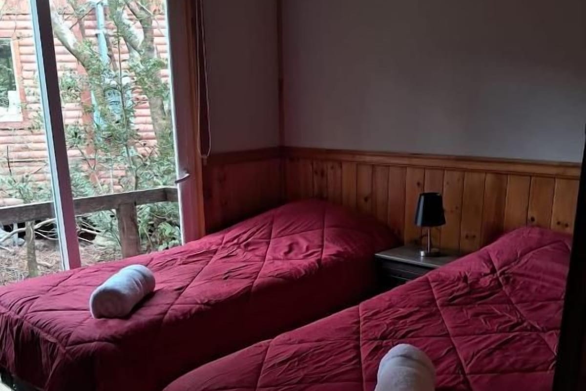 Habitació amb dos llits, una finestra i una tauleta de nit amb una làmpada.