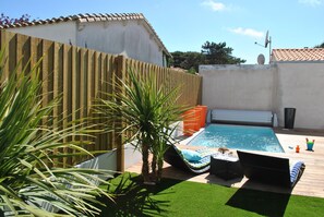 Un patio trasero con piscina, terraza de madera y área cercada.