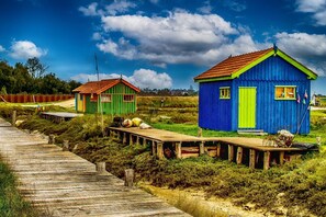 Un muelle de madera conduce a cabañas de madera coloridas, con un paisaje cubierto de césped y un cielo despejado.