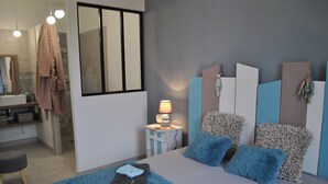 Ett modernt sovrum med en säng, ett sängbord med en lampa, en spegel och ett badrum som syns i bakgrunden.