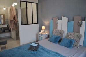 Un dormitorio moderno con cama, mesita de noche con lámpara, espejo y baño visible al fondo.