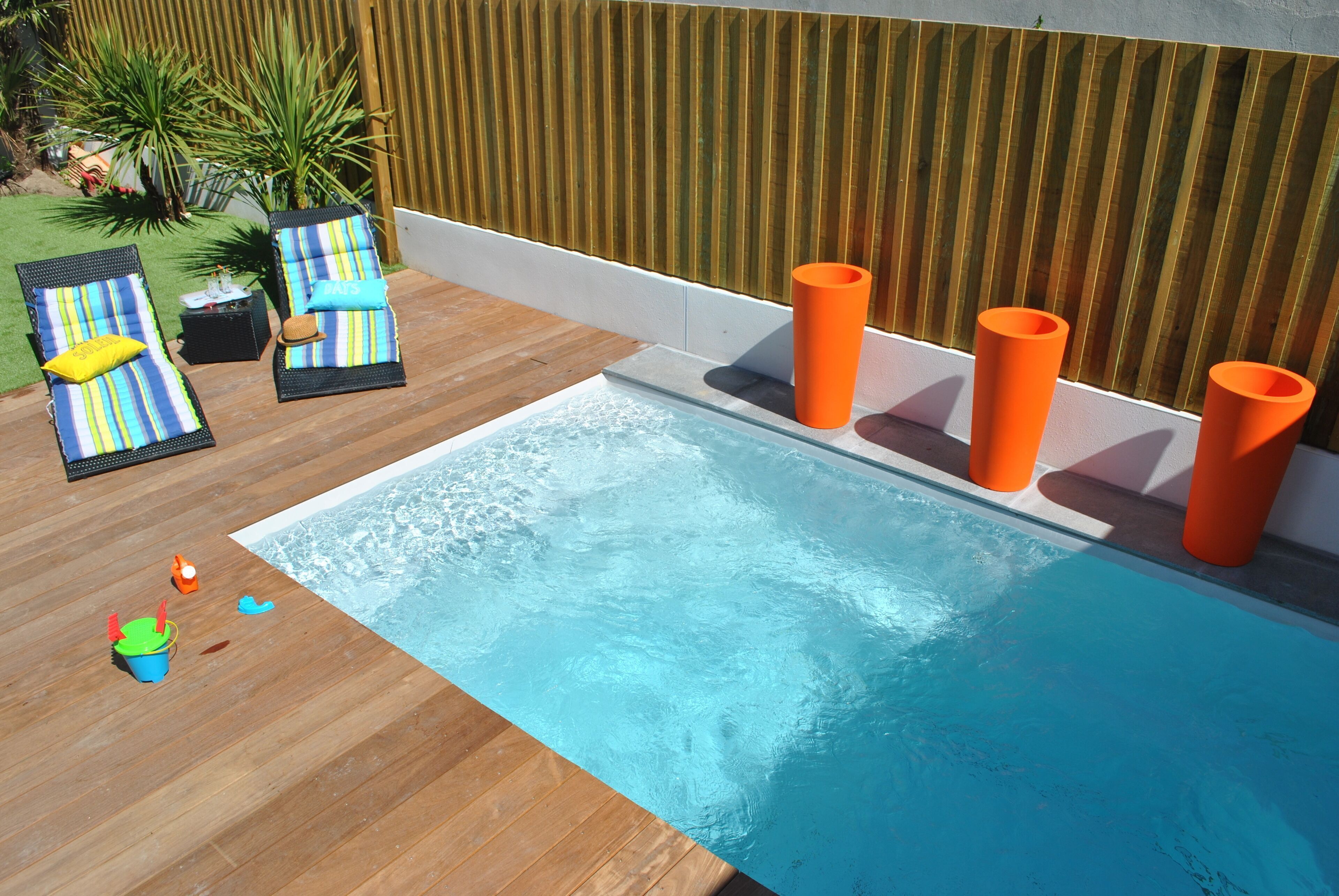 A swimming pool with lounge chairs and orange cylindrical objects.