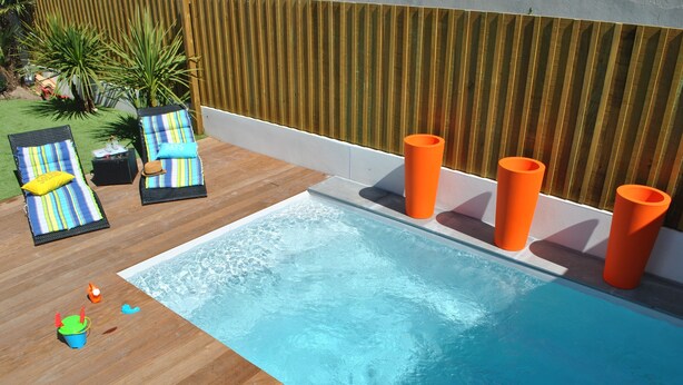 En swimmingpool med solstolar och orange, cylinderformade föremål.