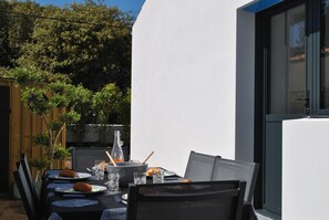 Un área de comedor al aire libre con una mesa dispuesta para dos personas, rodeada de sillas, un cerco de madera y una botella de vidrio.