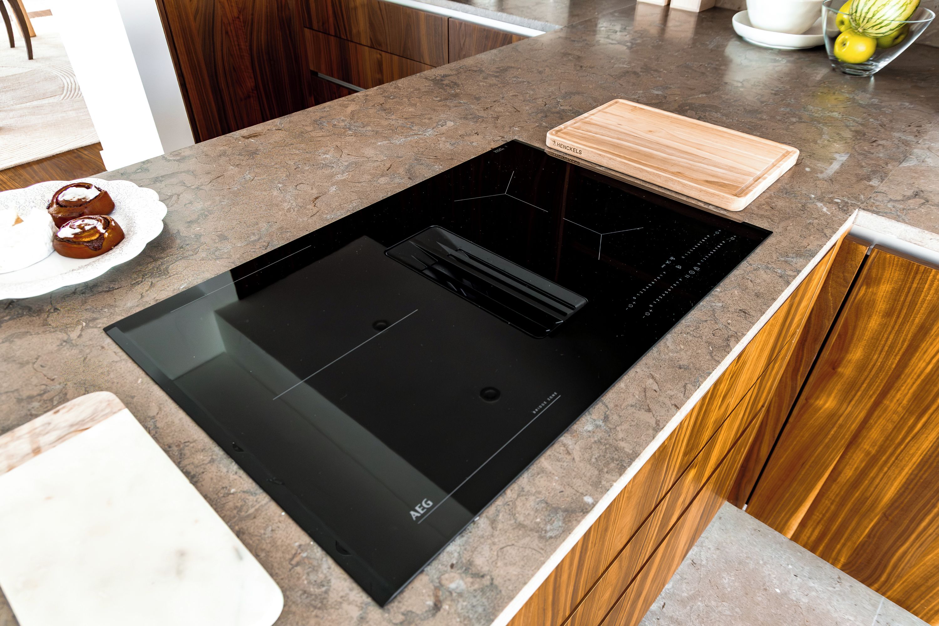 Une cuisine dotée d’une plaque de cuisson à induction noire, de meubles en bois et d’une assiette blanche contenant de la nourriture.
