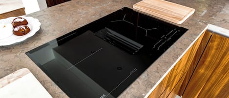 A kitchen with a black induction cooktop, wooden cabinets, and a white plate with food.