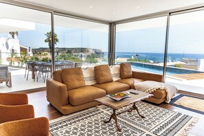 A modern living room with a sofa, a coffee table, and a view of the sea. - Villa 911 · Heated pool &Unique View in Praia da luz (Luz)