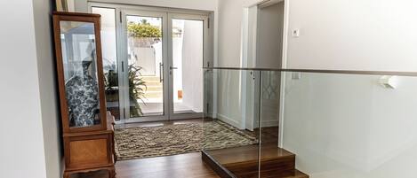 A modern interior with a wooden staircase, glass railings, and a patterned rug.