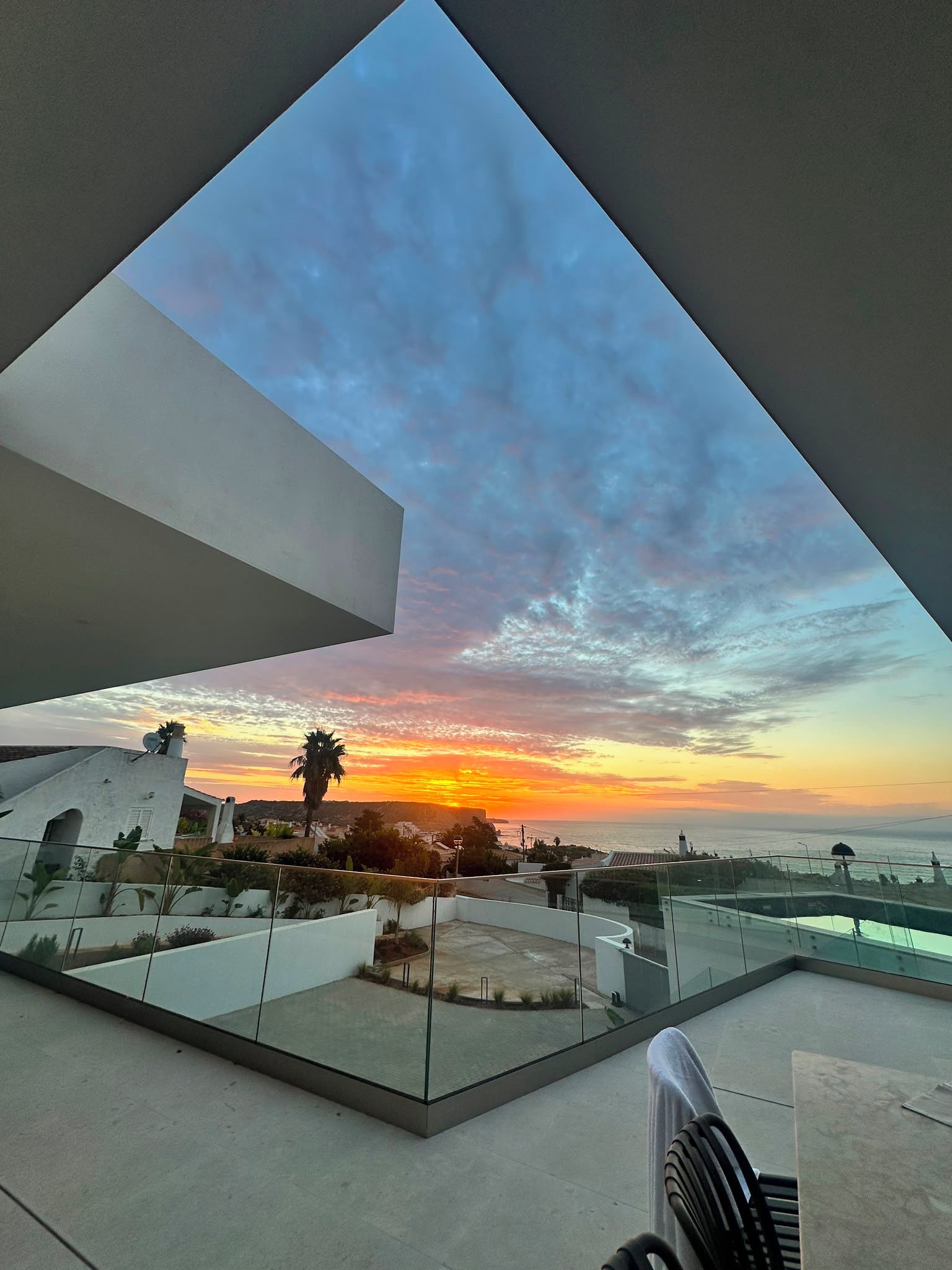 A modern building with a glass balcony overlooking a sunset.