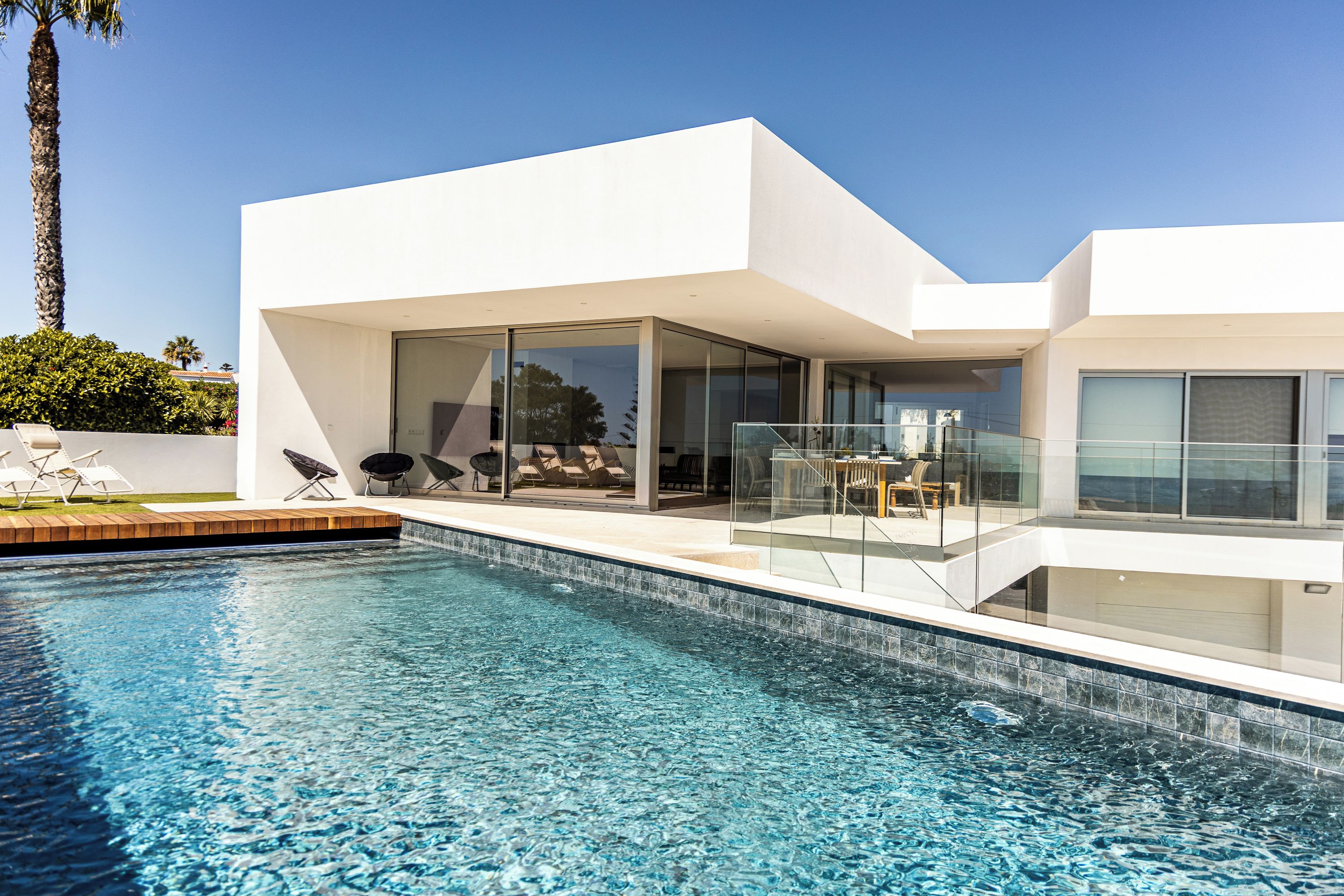 Una casa moderna con piscina, puertas de cristal y mobiliario de exterior.