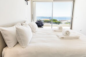 A hotel room with a bed, pillows, a folded towel, a chair, and a view of the sea through a glass door. - Villa 911 · Heated pool &Unique View in Praia da luz (Luz)
