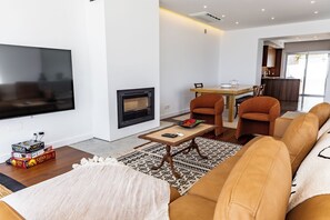 Ein modernes Wohnzimmer mit Flachbildfernseher, Kamin, Essbereich mit Tisch und Stühlen sowie einer Couch.