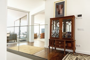 Een moderne woonkamer met een glazen schuindeur naar een balkon, een houten kast met glazen deuren en een ingelijst kunstwerk aan de muur.