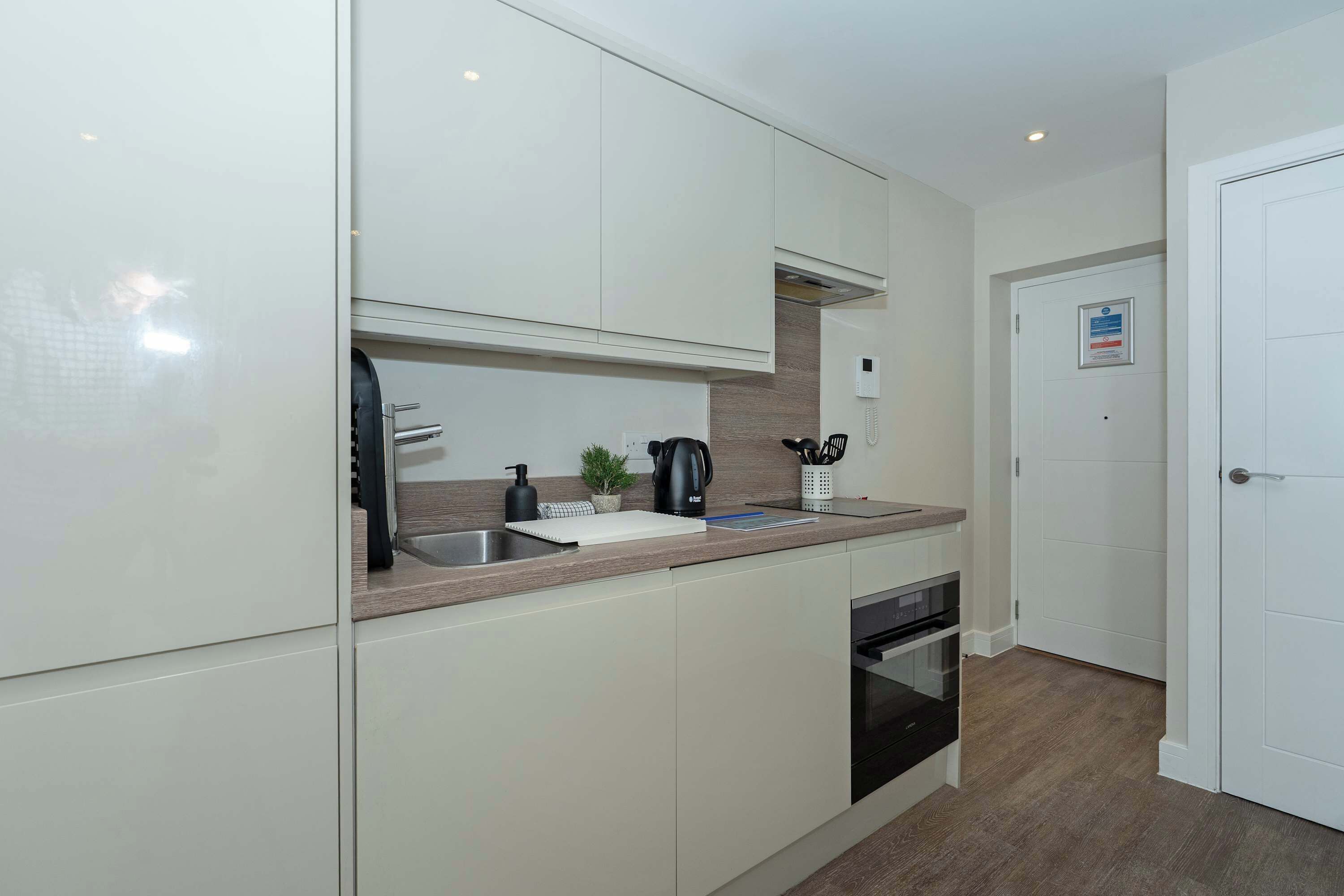 A modern kitchen with white cabinets, a stainless steel sink, a black coffee maker, and a built-in oven.
