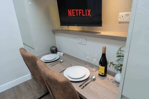 A neatly arranged dining area with a television displaying the Netflix logo, a bottle of wine, and a 'NO SMOKING' sign. - Smart and Stylish Twin Bed Studio (Southampton)