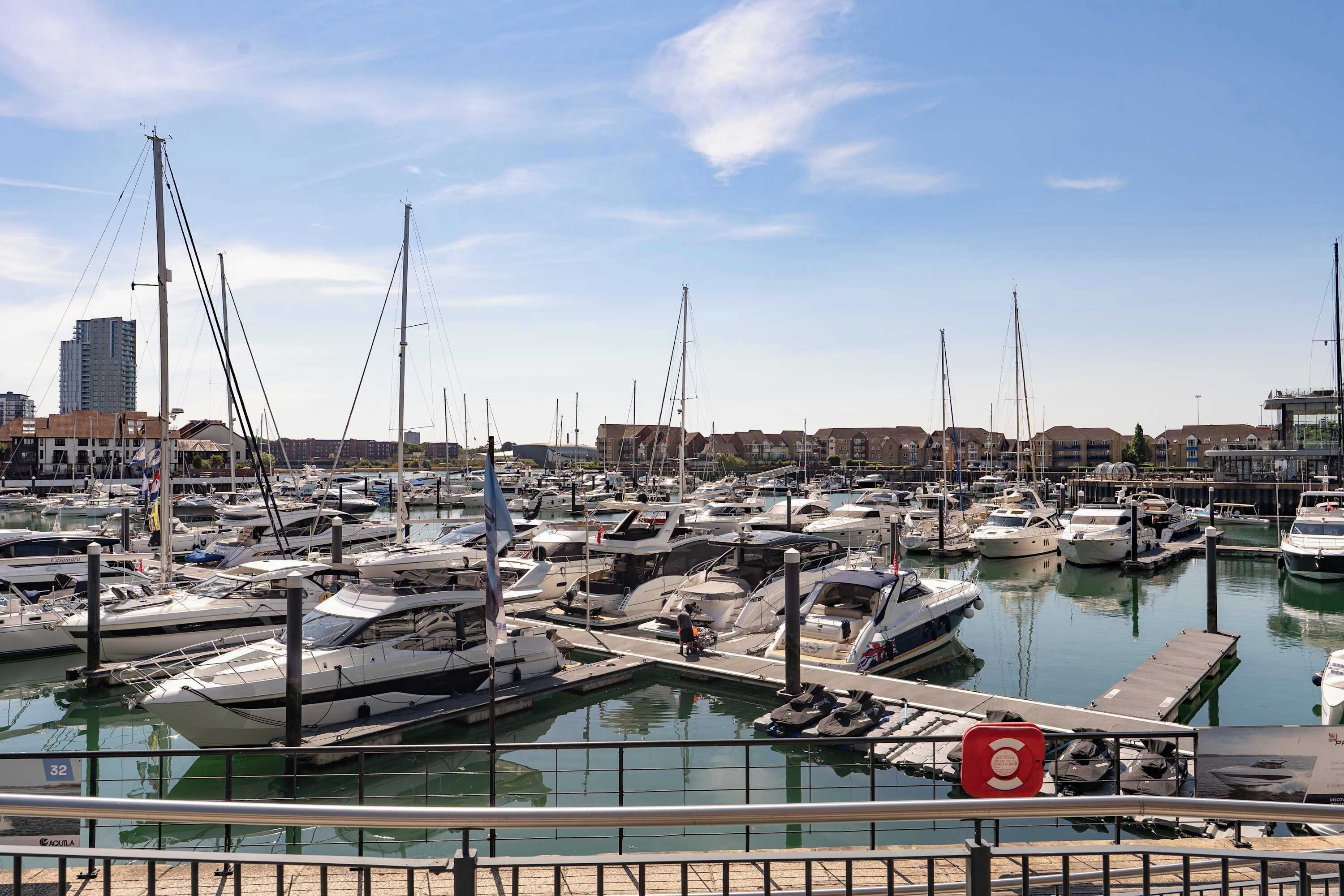 A marina with numerous boats docked, a clear sky, and buildings in the background.