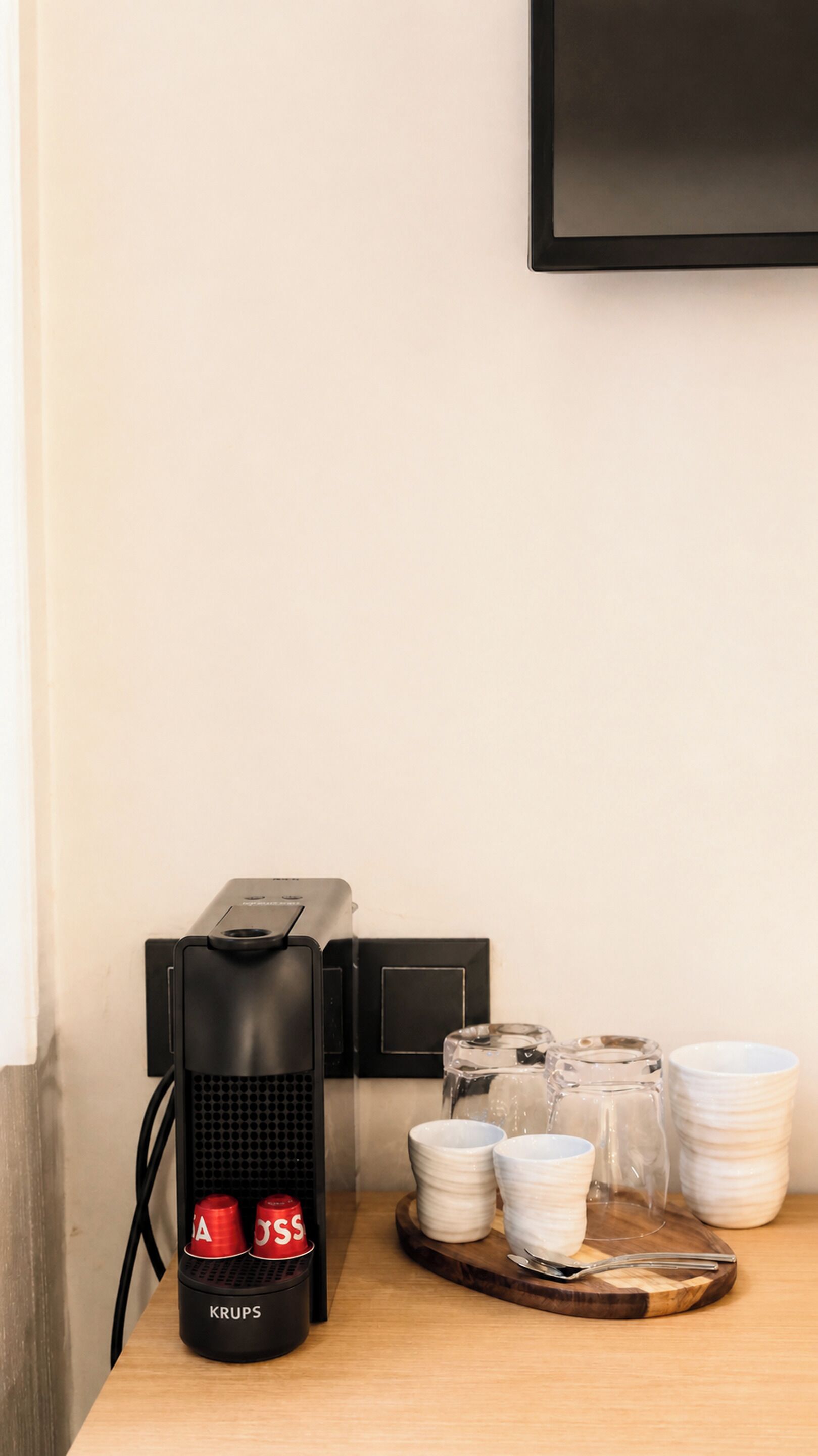 A coffee machine with two red cups, a stack of white plates, and a tray with cups and a glass on a wooden surface.