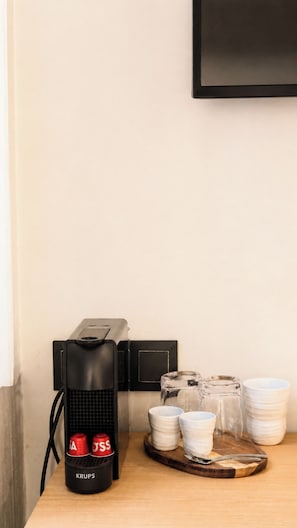 A coffee machine with two red cups, a stack of white plates, and a tray with cups and a glass on a wooden surface. - Hotel Casa Beatas (Malaga)