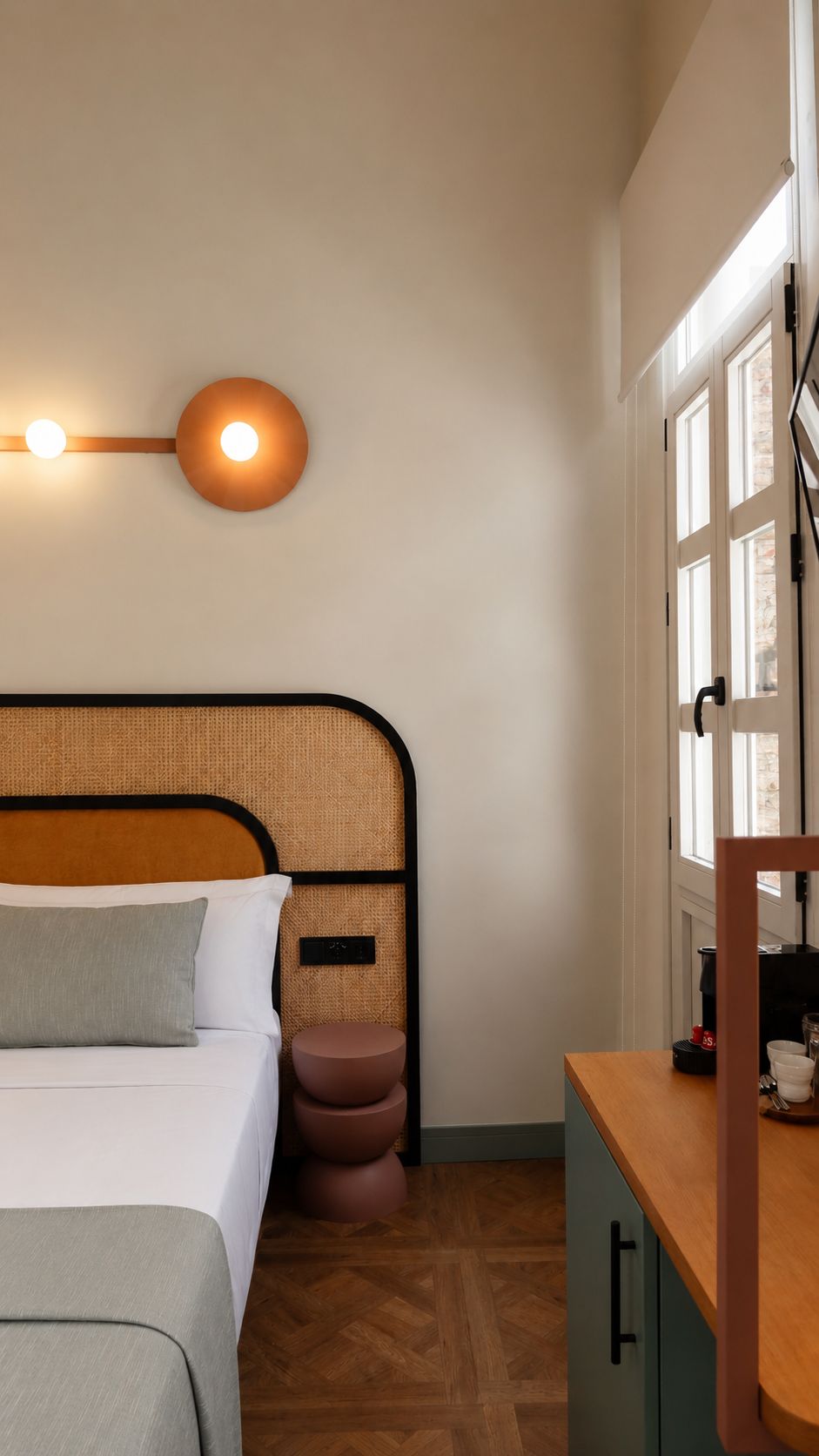 Un dormitorio con cama, mesita de noche, lámpara de pared y ventana con vistas.