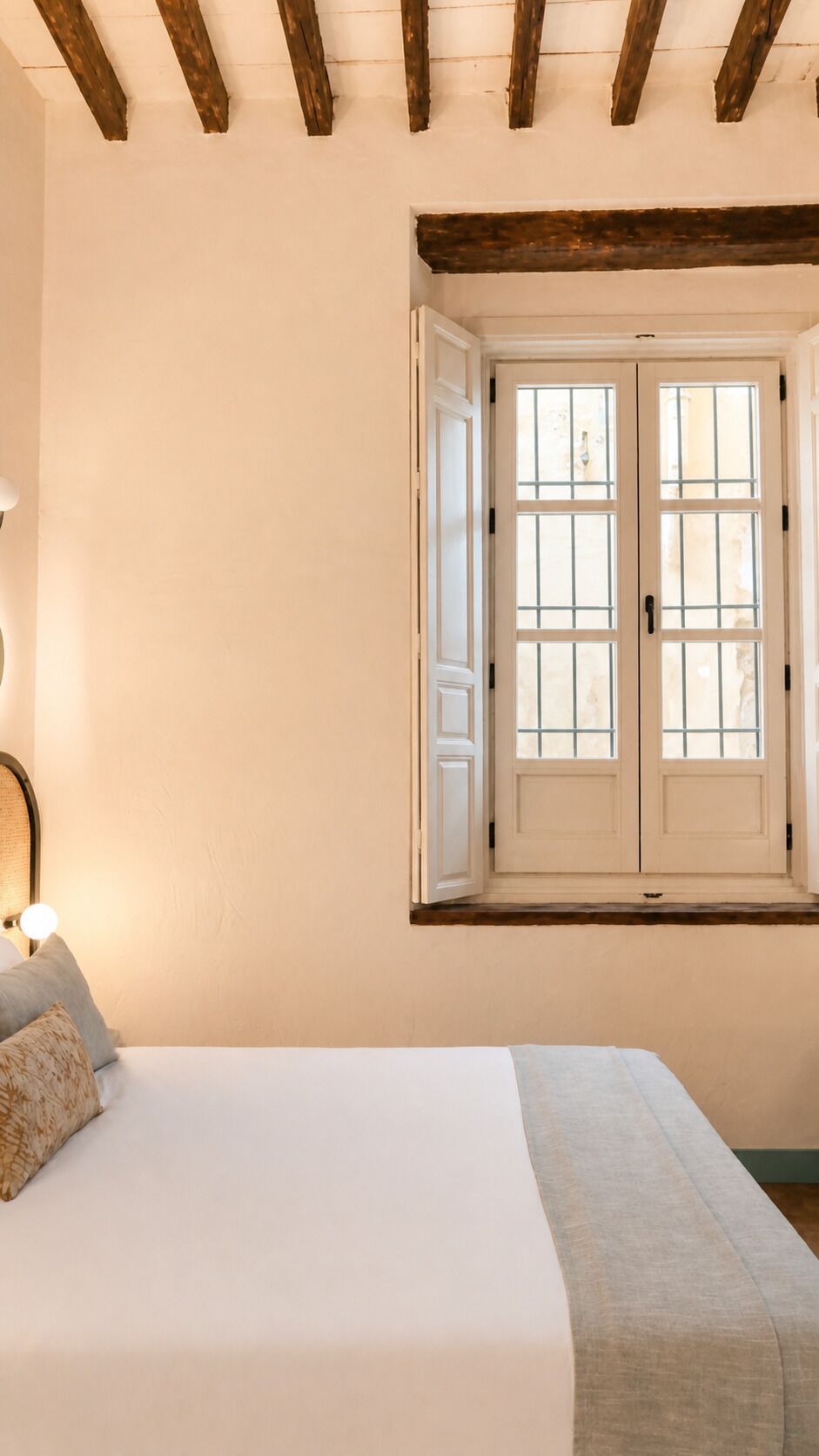 Ein Schlafzimmer mit einem Bett, einem Fenster mit weißen Fensterläden und einem Holzbalken an der Decke.