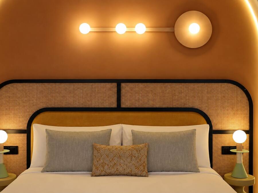 A bed with a headboard featuring a woven pattern, two bedside lamps, and a wall-mounted light fixture above the bed.