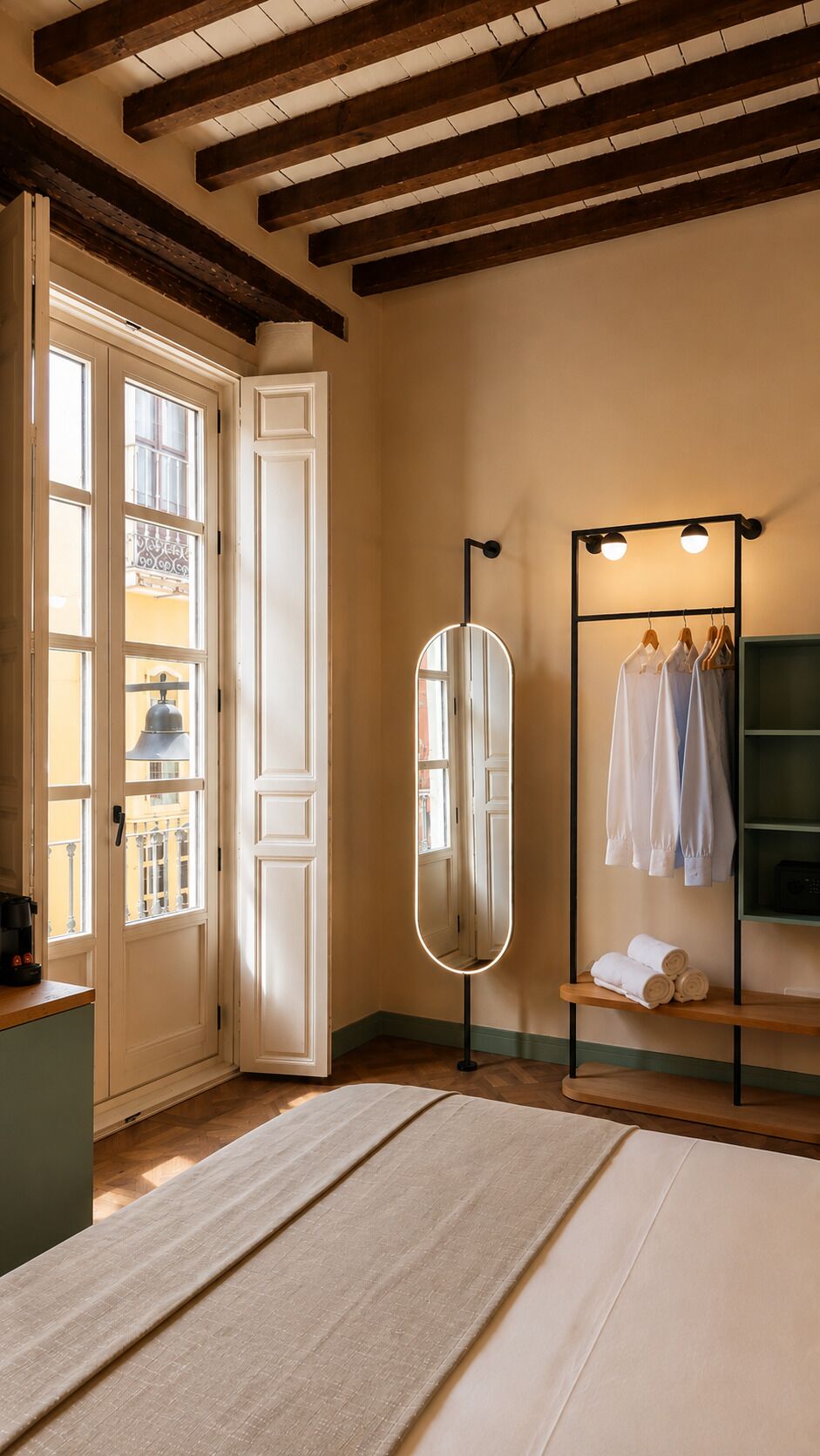 Un dormitorio con techo de madera, un espejo grande, un armario con ropa colgada y una cama con colcha color beige.