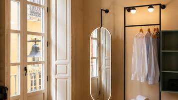 Un dormitorio con techo de madera, un espejo grande, un armario con ropa colgada y una cama con colcha color beige.
