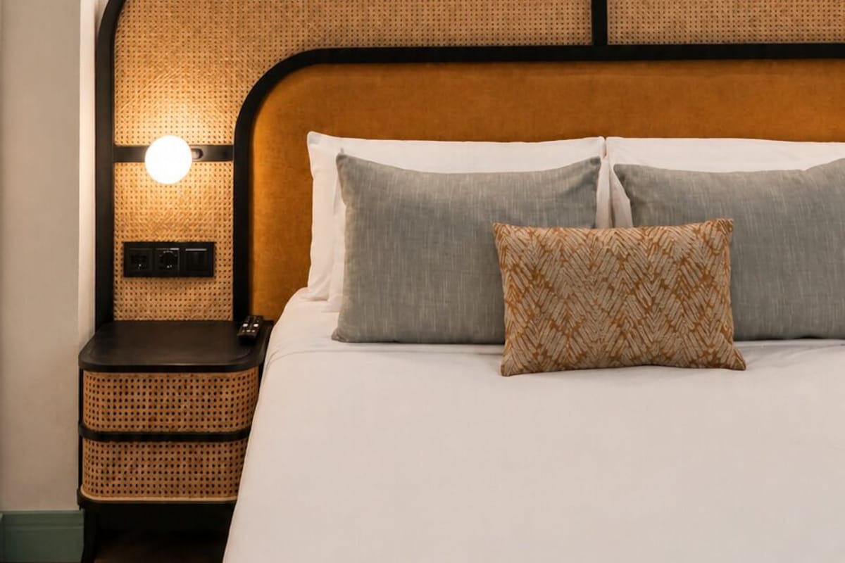 A bedroom with a bed, a headboard with a woven design, and wall-mounted lights.