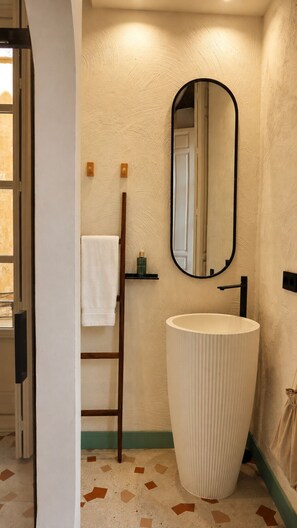 Un baño con un lavabo grande con textura, un espejo y un perchero para toallas.