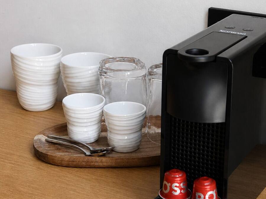 Una macchina da caffè con base nera e tazze rosse, un vassoio di legno con tazze bianche impilate e un bicchiere di vetro trasparente.