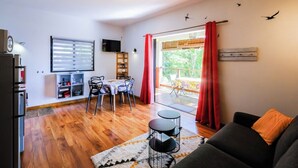 Sala de estar com sofá, mesa de jantar com cadeiras, televisão e varanda com cortinas vermelhas.