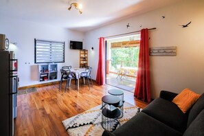 Een woonkamer met een bank, een eettafel met stoelen, een televisie en een balkon met rode gordijnen.
