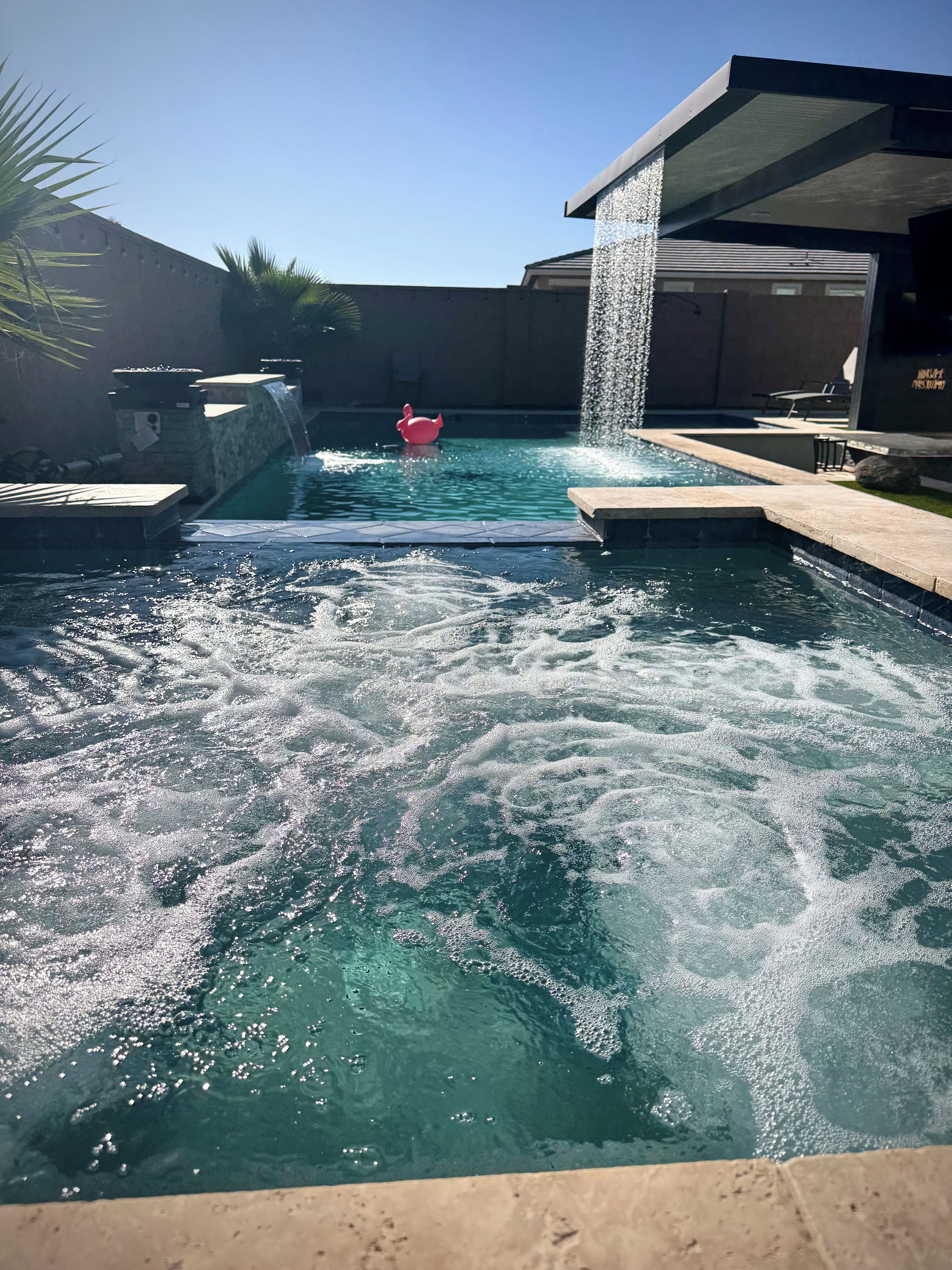 A swimming pool with a waterfall feature, a red duck float, and a stone wall.