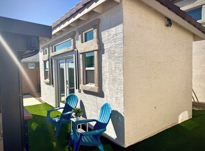 A house with a patio area featuring two blue chairs and a small table, a sliding glass door, and a window with a view of the sky. - Spacious 5-bedroom house in marvelous Maricopa with AC (Maricopa)