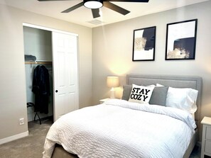 A bedroom with a bed, a ceiling fan, a bedside lamp, and two framed pictures on the wall. - Spacious 5-bedroom house in marvelous Maricopa with AC (Maricopa)