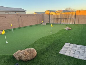 A backyard with artificial green turf, a wooden fence, and a paved walkway. - Spacious 5-bedroom house in marvelous Maricopa with AC (Maricopa)