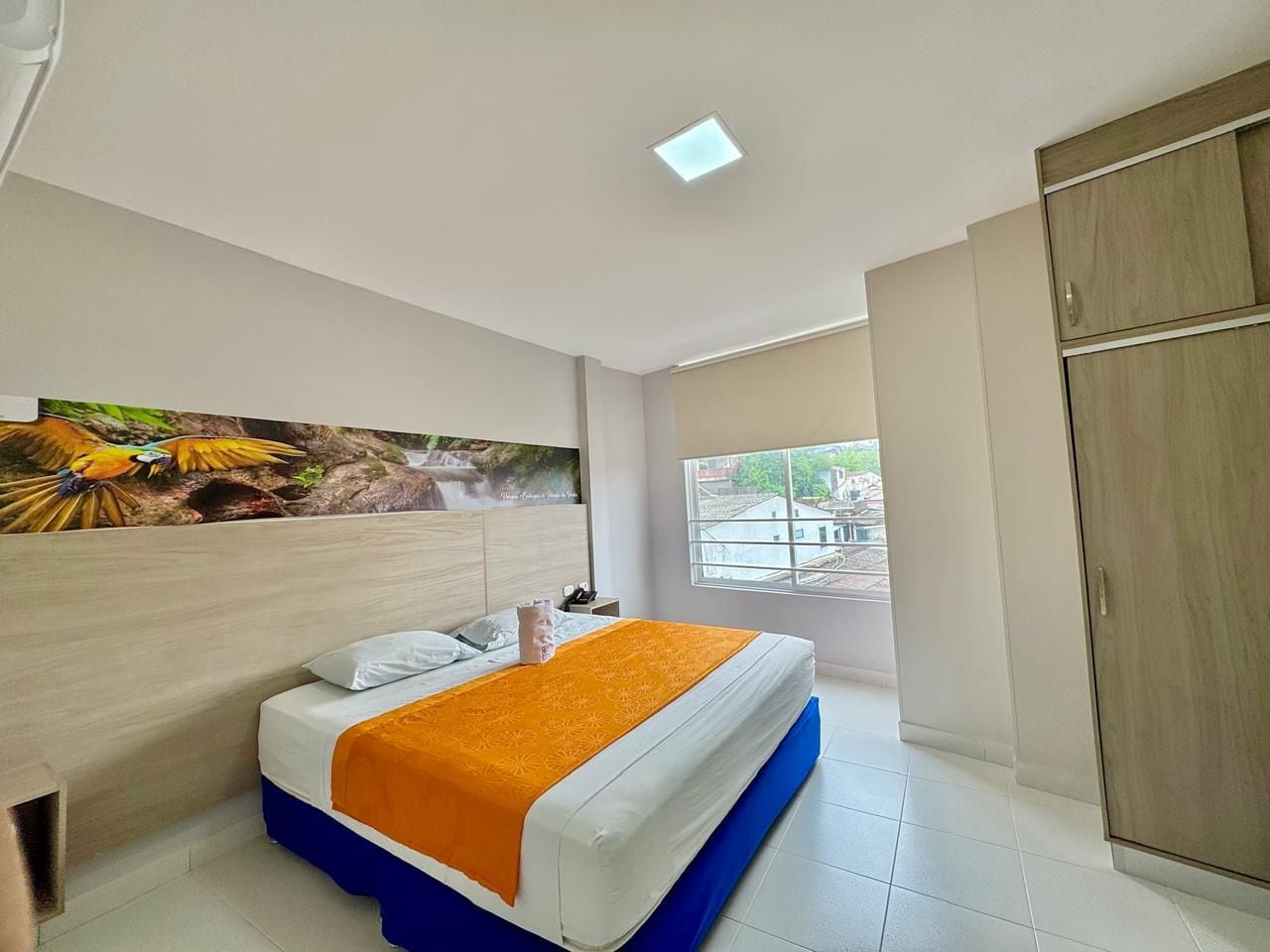 Una habitación de hotel con cama, ventana, armario y un cuadro en la pared.