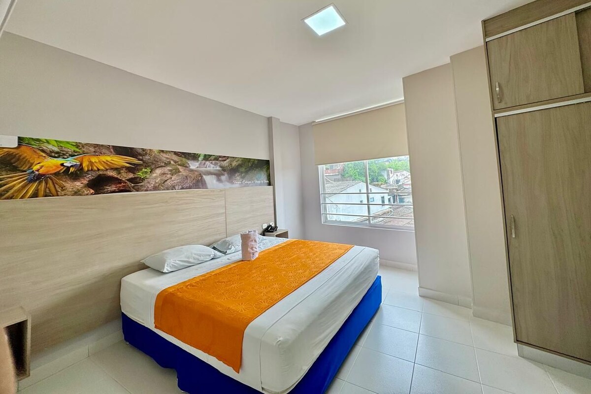 Una habitación de hotel con cama, ventana, armario y un cuadro en la pared.