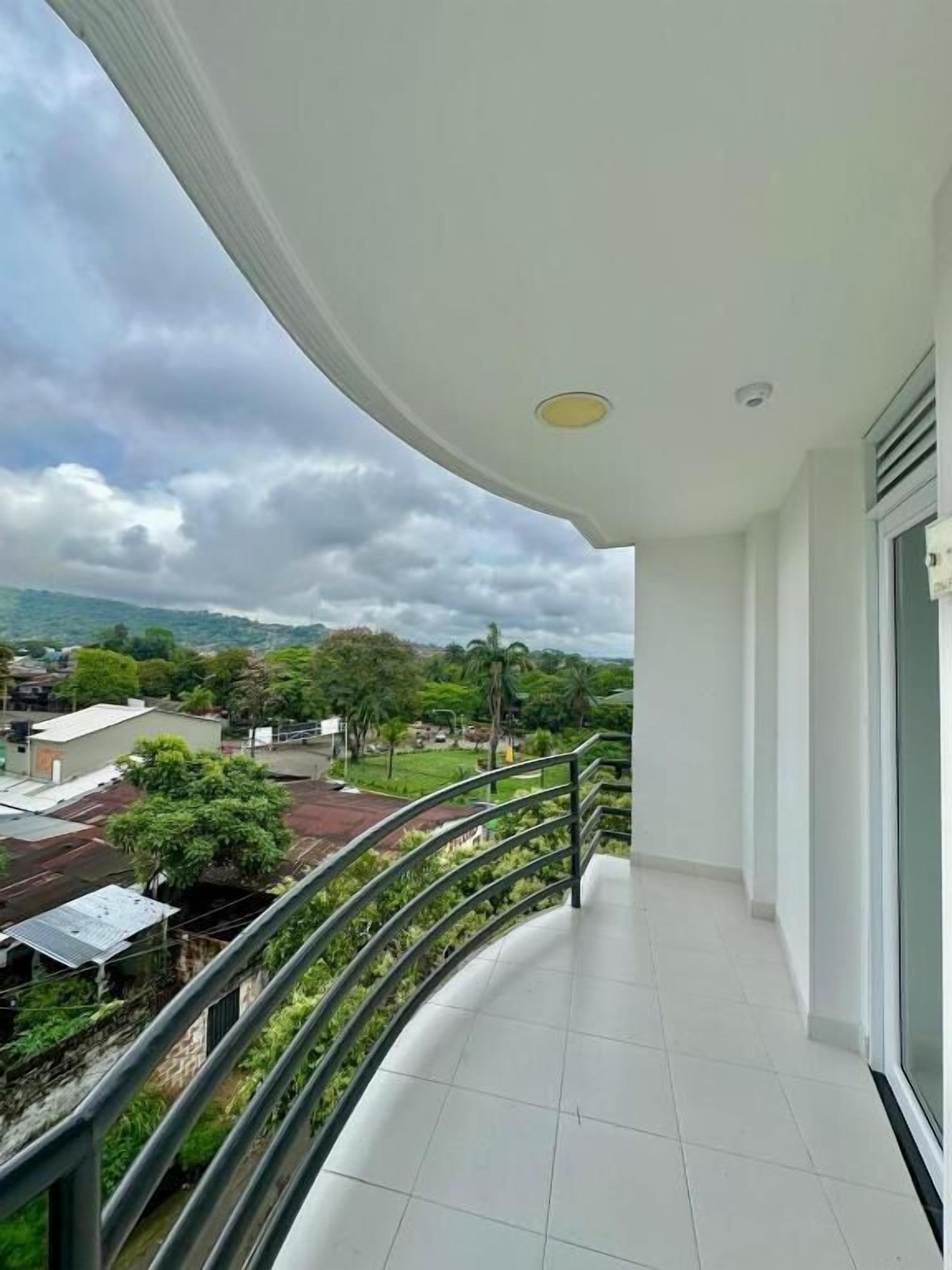 Ein Balkon mit gebogener Geländer, Fliesenboden und Blick auf ein Wohngebiet mit Häusern und Bäumen.